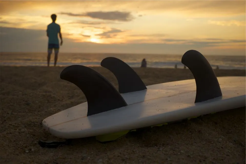 Tabla de surf con sus quillas sobre la arena de la playa al atardecer